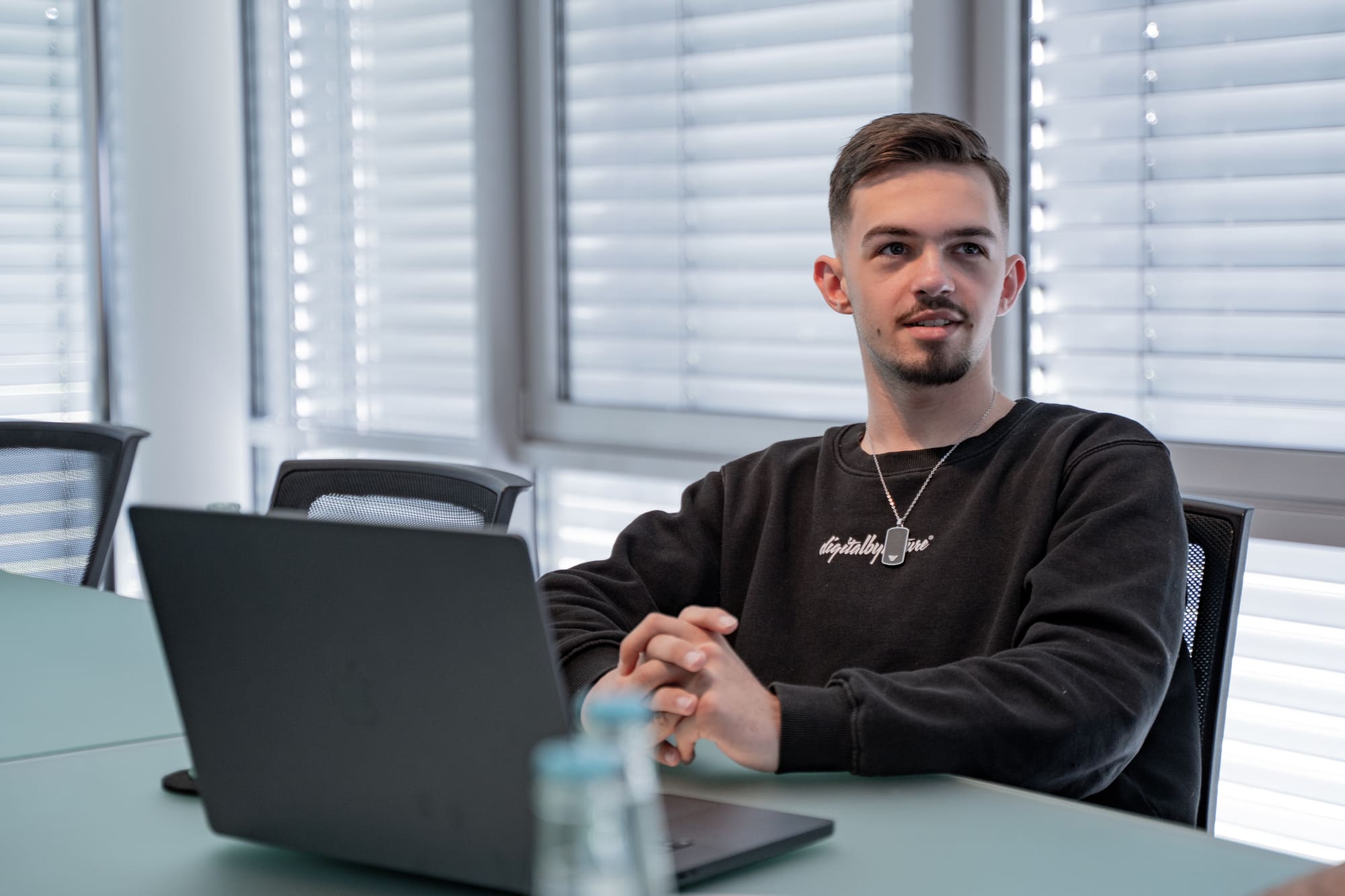 Joel aus dem Team von digitalbynature im Meetingraum am Laptop, mit digitalbynature-Pullover